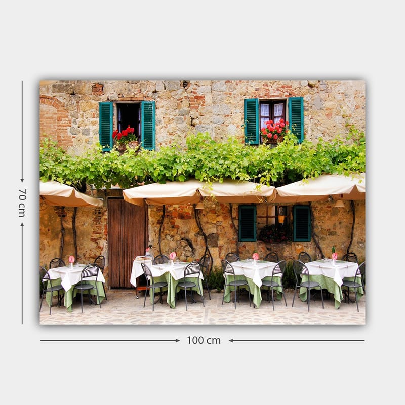 Canvastavla 70x100 cm - Charmig uteservering med vita bord och gröna dukar framför en gammal stenbyggnad med fönsterluckor i mörkgrön färg - Mörkgrön / Vit / Tegelröd - Inredning & dekor - Tavlor & konst - Canvastavla