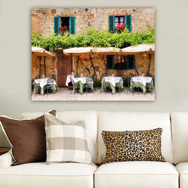 Canvastavla 70x100 cm - Charmig uteservering med vita bord och gröna dukar framför en gammal stenbyggnad med fönsterluckor i mörkgrön färg - Mörkgrön / Vit / Tegelröd - Inredning & dekor - Tavlor & konst - Canvastavla