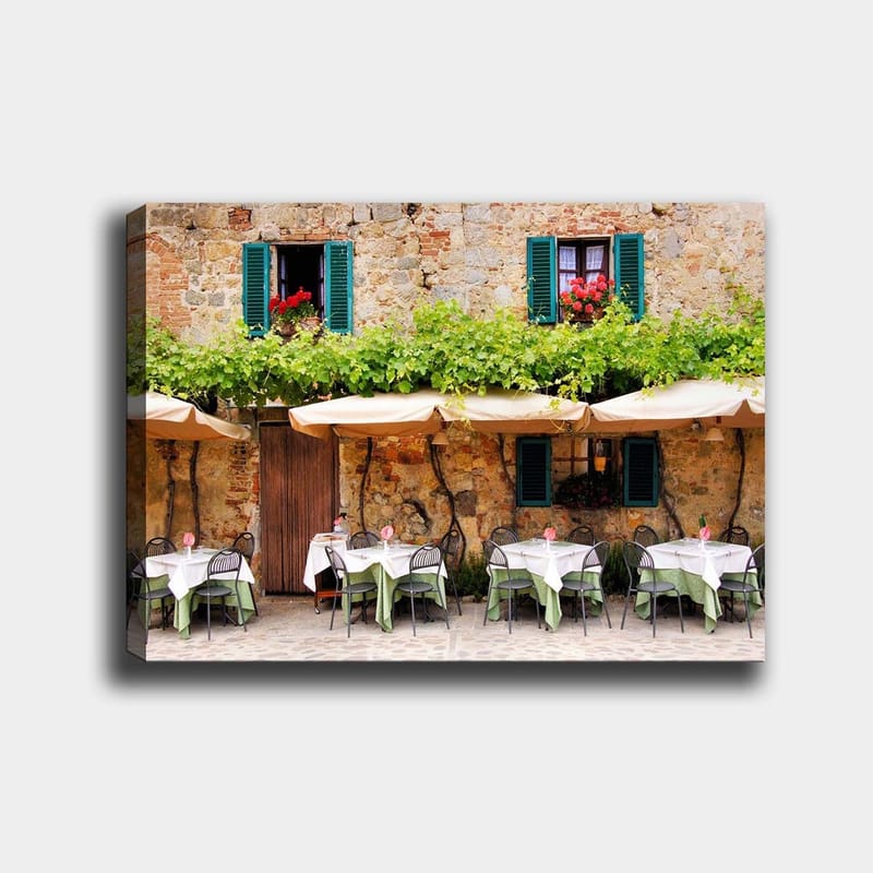 Canvastavla 70x100 cm - Charmig uteservering med vita bord och gröna dukar framför en gammal stenbyggnad med fönsterluckor i mörkgrön färg, Mörkgrön / Vit / Tegelröd