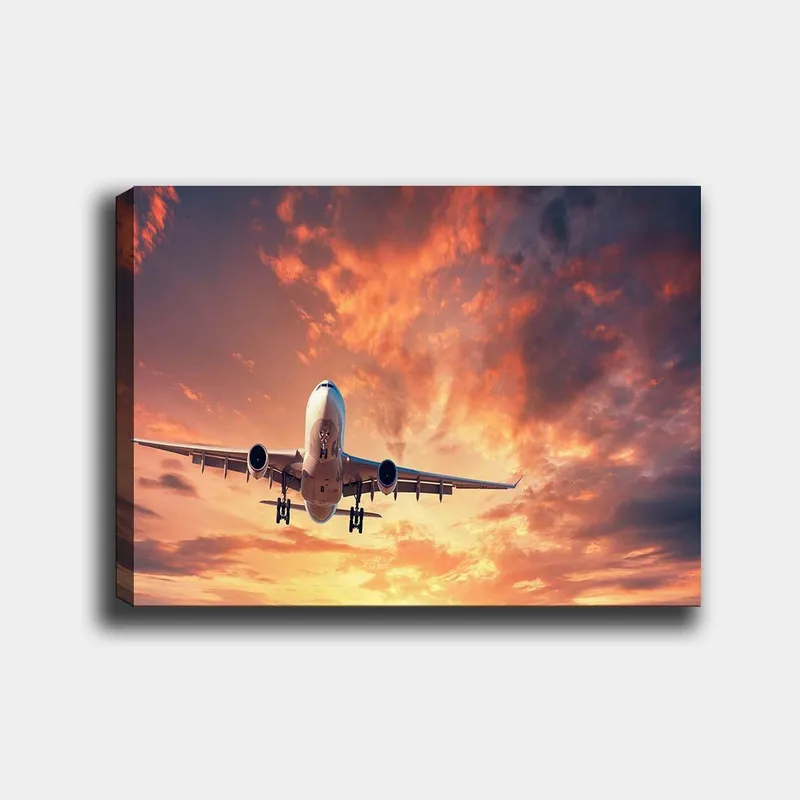 Canvastavla 70x100 cm - Ett flygplan som landar mot en dramatisk solnedgång med färgglada moln, Orange / Lila / Blå