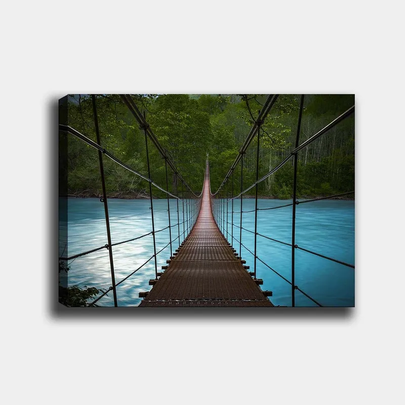 Canvastavla 70x100 cm - Hängbro som sträcker sig över en stilla, blå flod omgiven av grönskande träd, Mörkbrun / Turkos / Grön
