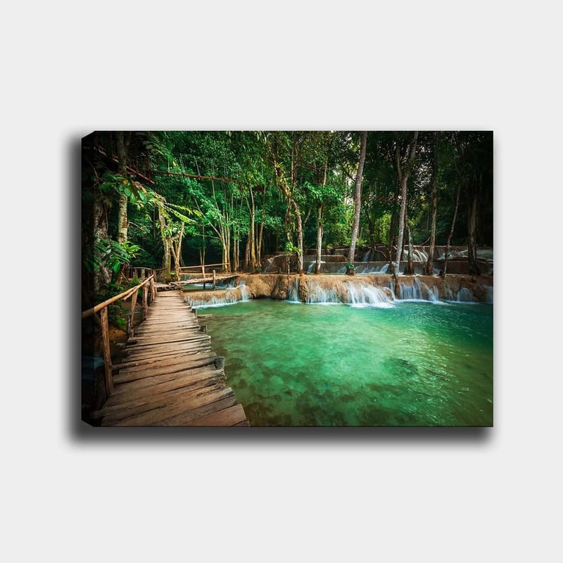 Canvastavla 70x100 cm - Lugn och naturskön plats med en träbro som leder över en klar, turkos vattenfallspool omgiven av frodig grönska, Turkos / Grön / Brun