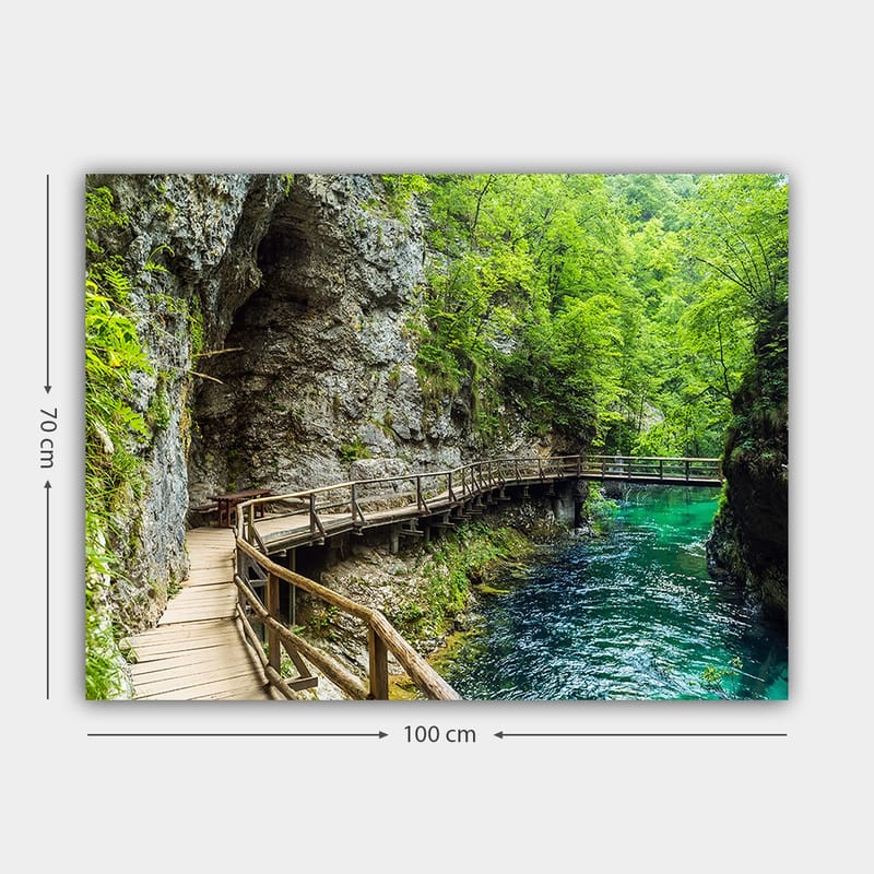 Canvastavla 70x100 cm - Naturskön vy av en träbro som slingrar sig genom en grönskande ravin vid en klar, turkos flod - Grön / Turkos / Grå - Inredning & dekor - Tavlor & konst - Canvastavla