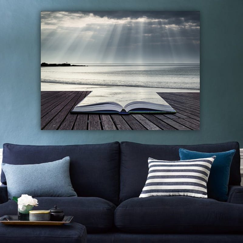 Canvastavla 70x100 cm - Öppen bok som ligger på en träbrygga vid havet, omgiven av mjuka ljusstrålar från en molnig himmel - Grå / Blå / Vit - Inredning & dekor - Tavlor & konst - Canvastavla