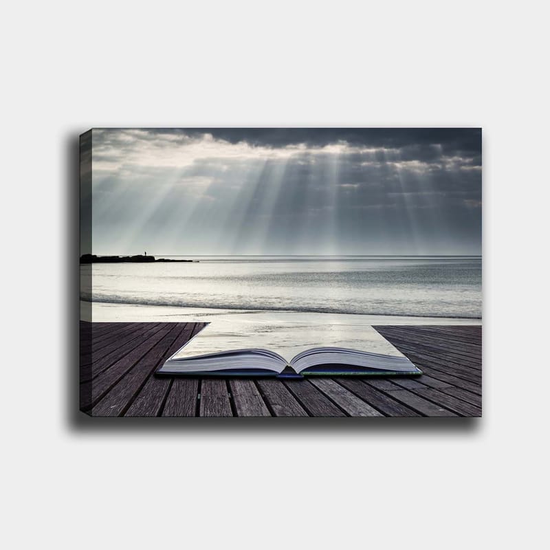 Canvastavla 70x100 cm - Öppen bok som ligger på en träbrygga vid havet, omgiven av mjuka ljusstrålar från en molnig himmel, Grå / Blå / Vit