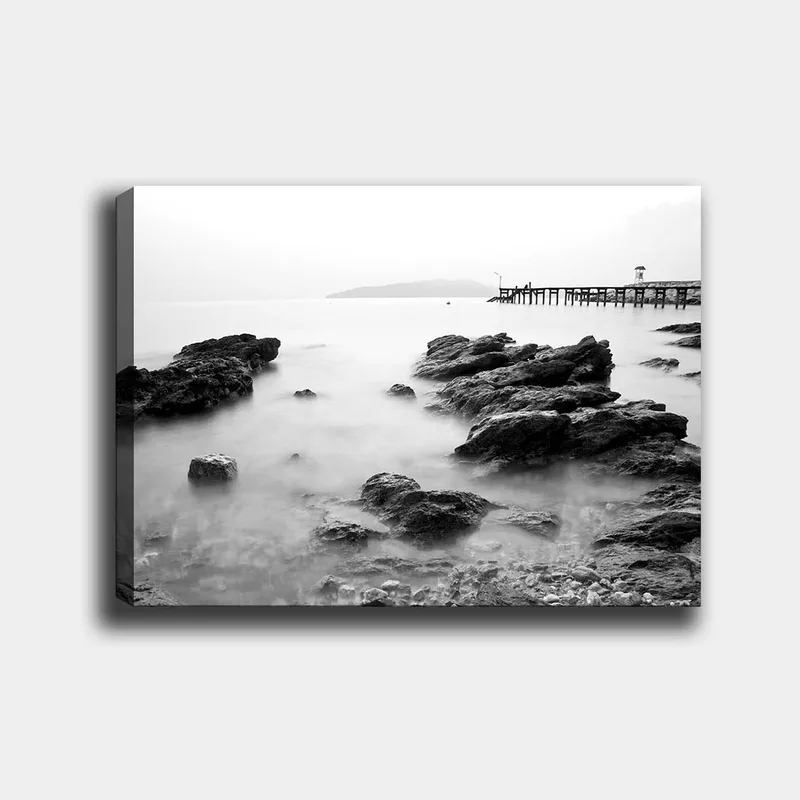Canvastavla 70x100 cm - Stillsam kustlandskap med klippor och en brygga i fjärran, Svart / Vitt / Grått