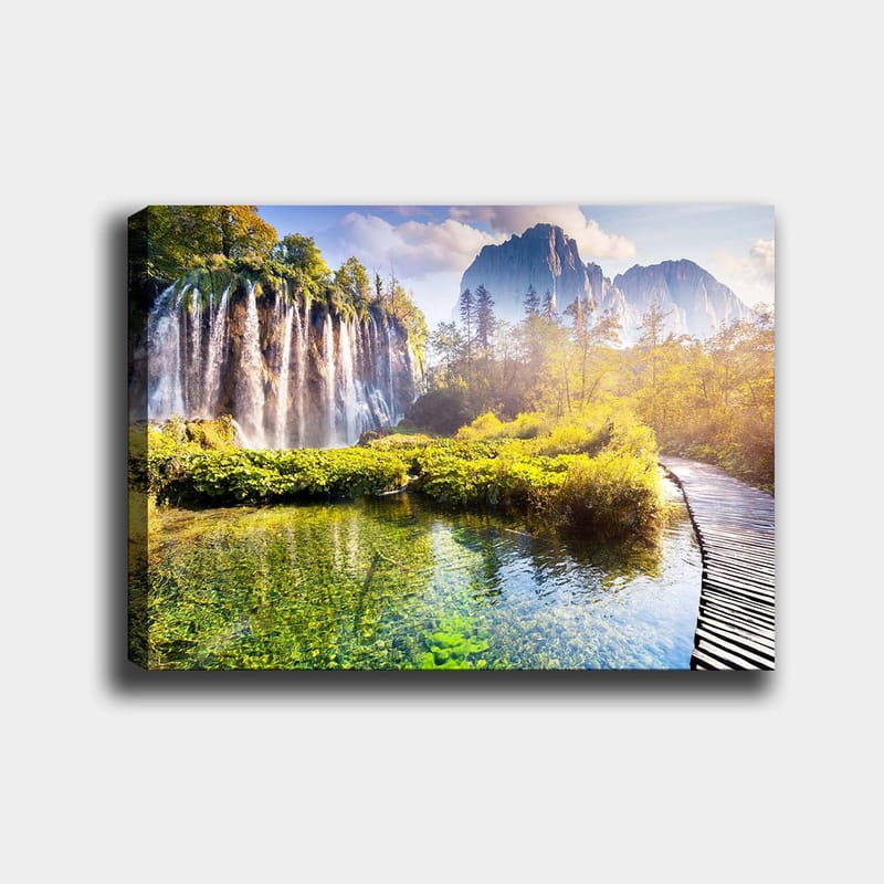 Canvastavla 70x100 cm - Storslagen vattenfallsscen omgiven av grönskande vegetation och majestätiska berg, Grön / Blå / Gul