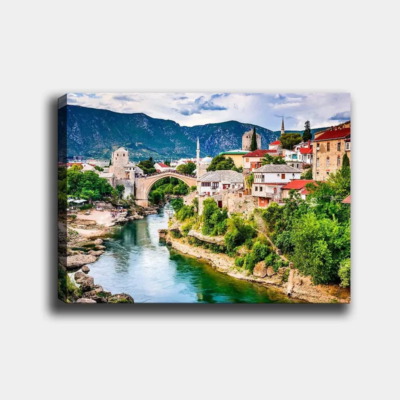 Canvastavla 70x100 cm - Vacker vy över en historisk bro som sträcker sig över en flod, omgiven av pittoreska hus och grönskande landskap, Grön / Blå / Röd
