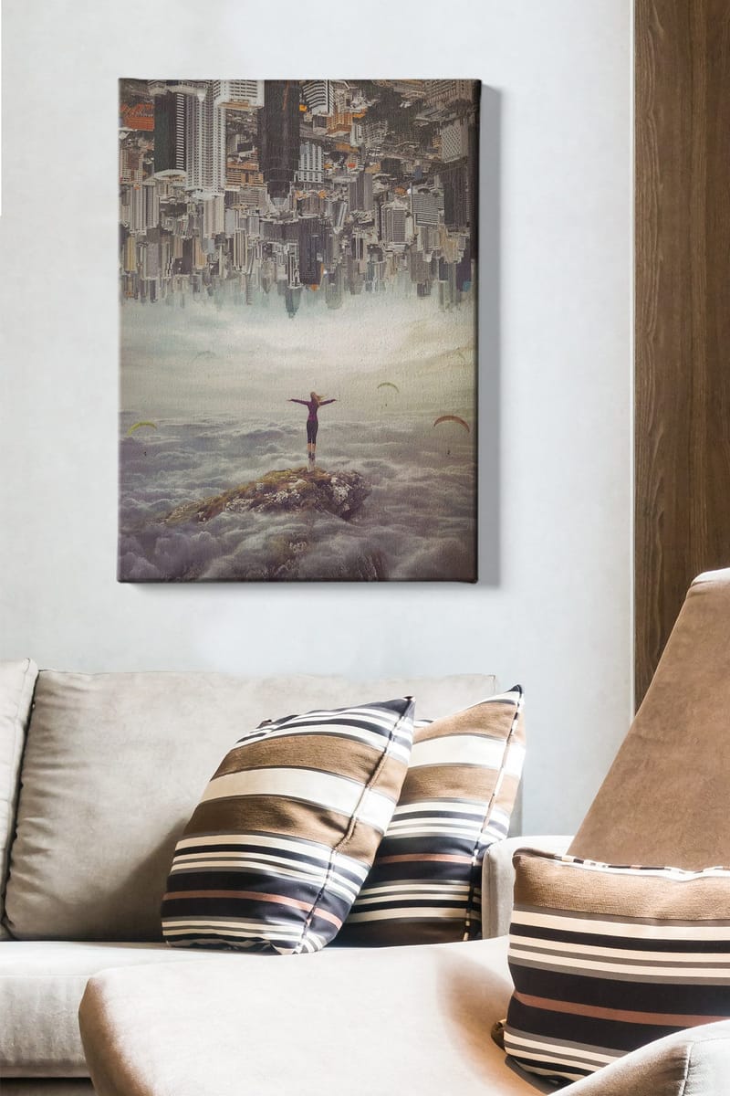 Canvastavla 70x100 cm - Person står med utsträckta armar på en klippa ovanför molnen, med en stad i bakgrunden som är upp och ner - Grå / Beige / Mörkblå - Inredning & dekor - Tavlor & konst - Canvastavla