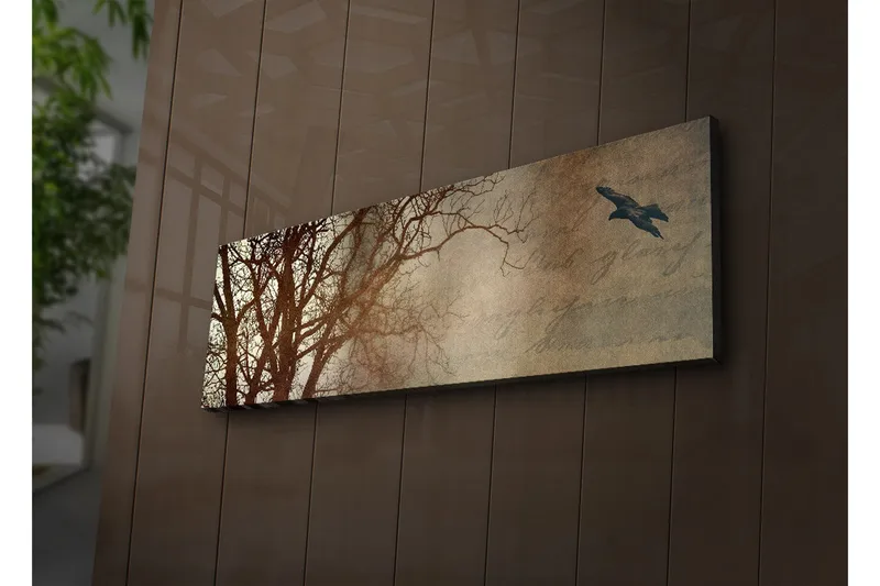 Canvastavla med LED-belysning 30x90 cm - Silhuett av träd med en fågel i flykt mot en mjukt tonad bakgrund, Mörkbrun / Beige / Svart